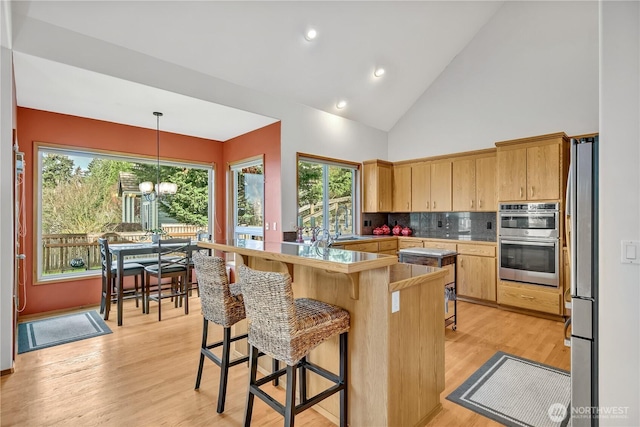 kitchen featuring a kitchen breakfast bar, appliances with stainless steel finishes, a chandelier, and light wood finished floors