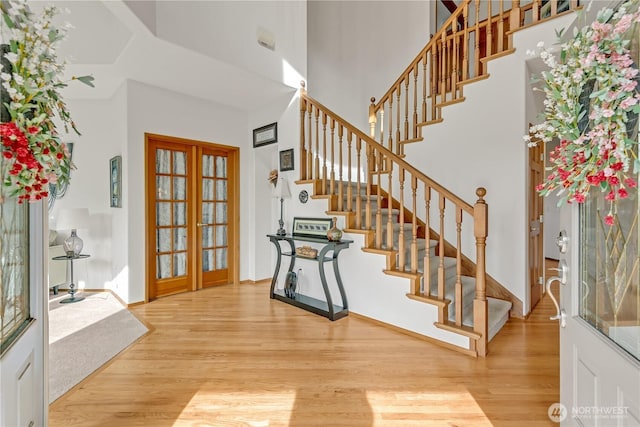 entrance foyer featuring stairs, a towering ceiling, wood finished floors, and french doors