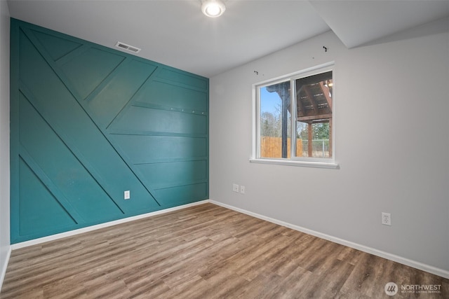 empty room featuring visible vents, baseboards, and wood finished floors