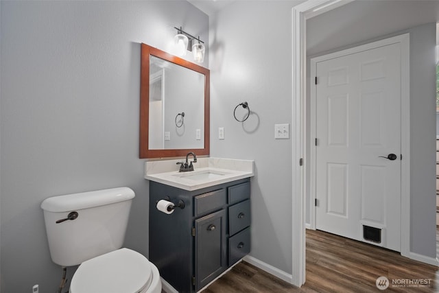 half bath with toilet, vanity, baseboards, and wood finished floors