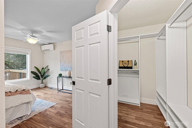 bedroom with a ceiling fan, wood finished floors, a textured ceiling, a wall mounted air conditioner, and baseboards