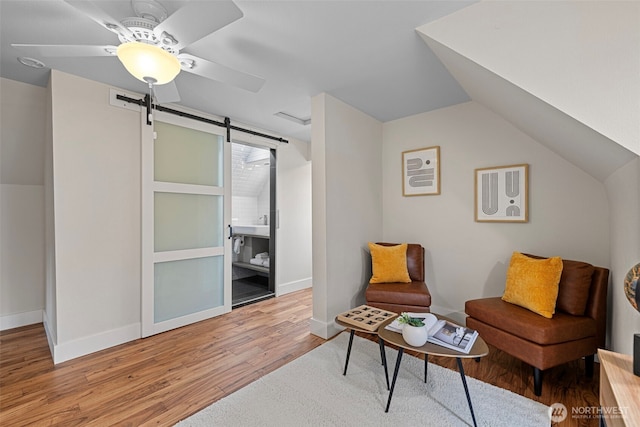 sitting room featuring a ceiling fan, a barn door, wood finished floors, lofted ceiling, and baseboards