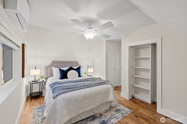 bedroom with baseboards, a wall mounted air conditioner, light wood-style flooring, and a ceiling fan