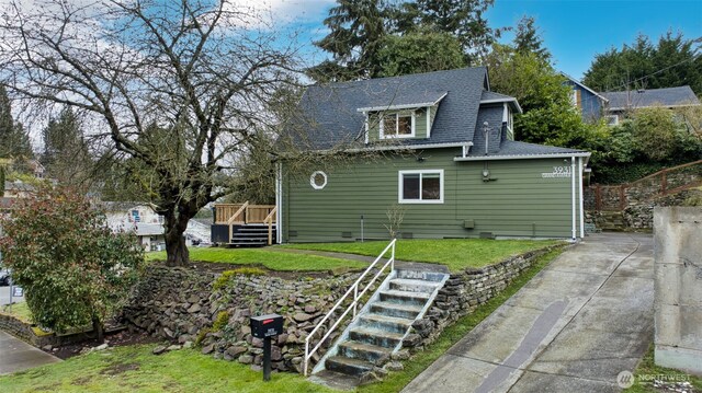 exterior space featuring concrete driveway, stairway, a wooden deck, a shingled roof, and a yard