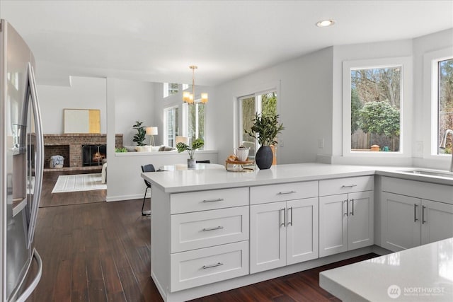 kitchen with dark wood-style flooring, stainless steel fridge with ice dispenser, a chandelier, a sink, and a peninsula
