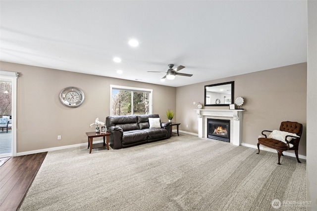 carpeted living area featuring a glass covered fireplace, recessed lighting, a ceiling fan, and baseboards