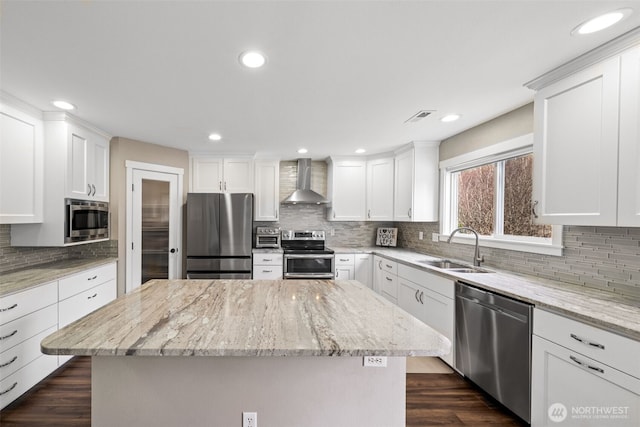 kitchen featuring a kitchen island, a sink, stainless steel appliances, white cabinets, and wall chimney exhaust hood