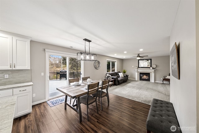 dining space with a glass covered fireplace, dark wood-type flooring, recessed lighting, and baseboards