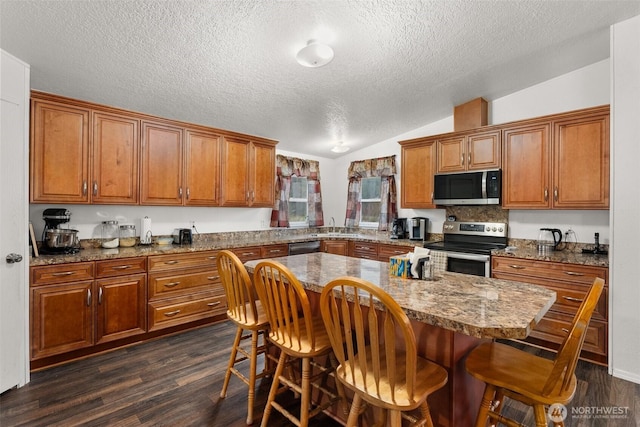 kitchen with dark wood-style flooring, brown cabinets, stainless steel appliances, and vaulted ceiling