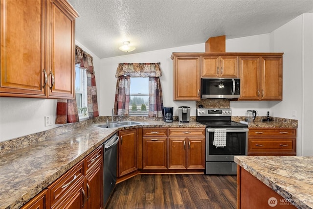 kitchen featuring dark wood finished floors, vaulted ceiling, appliances with stainless steel finishes, brown cabinetry, and a sink