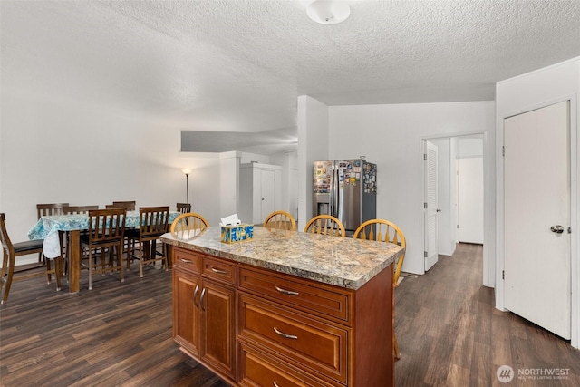 kitchen with dark wood-type flooring, brown cabinetry, stainless steel refrigerator with ice dispenser, and a center island