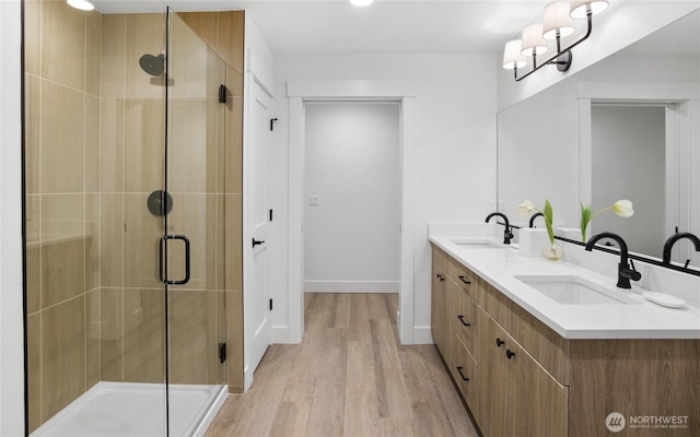 full bath featuring a sink, wood finished floors, a stall shower, and double vanity