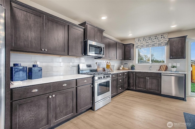 kitchen with dark brown cabinets, light countertops, decorative backsplash, appliances with stainless steel finishes, and light wood-style floors