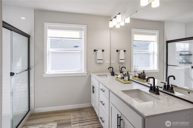 bathroom featuring a tile shower, baseboards, wood finished floors, and a sink