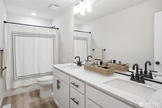 full bathroom with double vanity, wood finished floors, toilet, and a sink