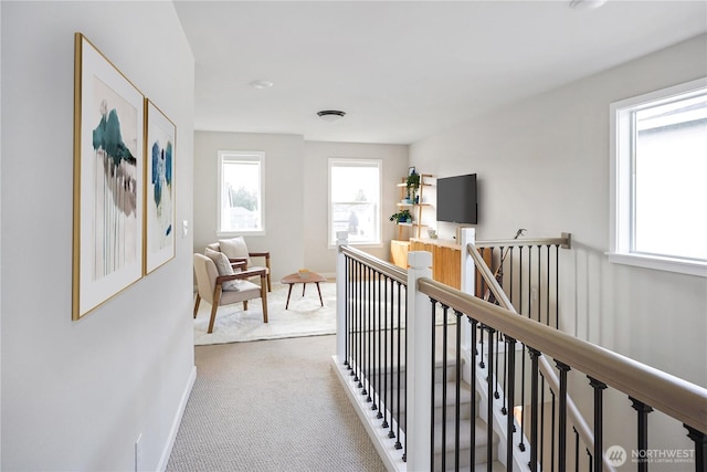 corridor featuring carpet, baseboards, an upstairs landing, and plenty of natural light
