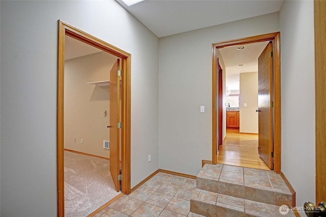 hall featuring light colored carpet, baseboards, and visible vents