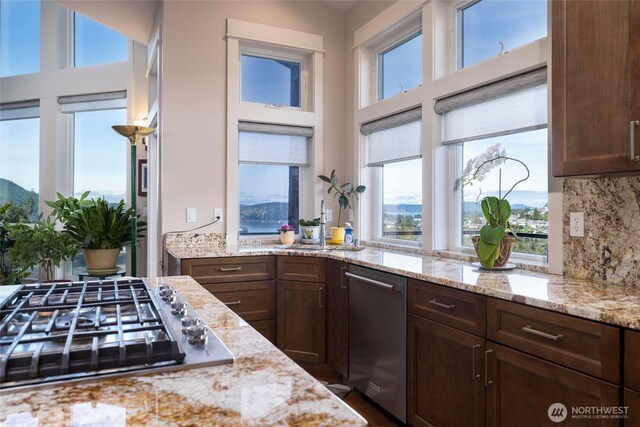 kitchen featuring dark brown cabinetry, stainless steel appliances, backsplash, and light stone counters
