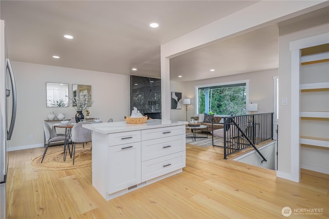 kitchen with white cabinets, light wood finished floors, light countertops, stainless steel fridge, and recessed lighting