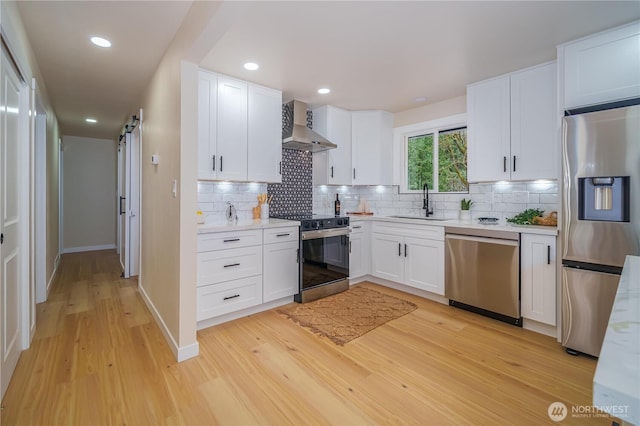 kitchen featuring stainless steel appliances, wall chimney range hood, light wood finished floors, tasteful backsplash, and a sink