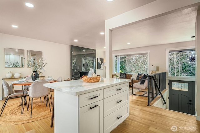 kitchen with light wood finished floors, light stone countertops, white cabinetry, recessed lighting, and a kitchen island