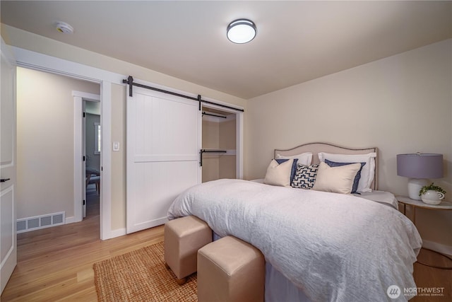 bedroom featuring light wood-type flooring, a barn door, baseboards, and a closet