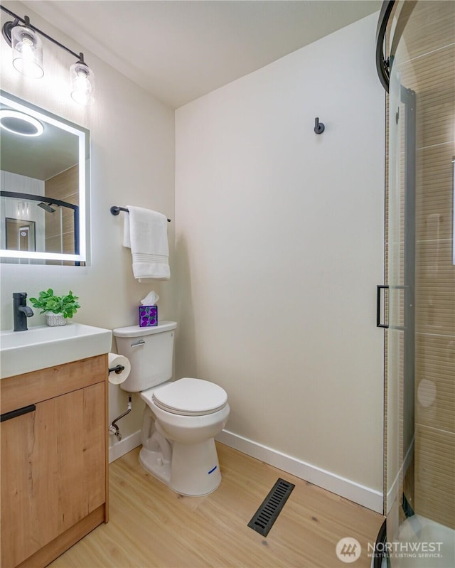bathroom featuring wood finished floors, baseboards, an enclosed shower, toilet, and vanity
