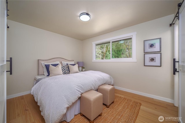 bedroom featuring light wood-style flooring, baseboards, and a barn door