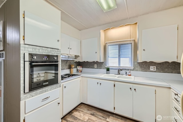 kitchen featuring tasteful backsplash, wall oven, under cabinet range hood, and a sink