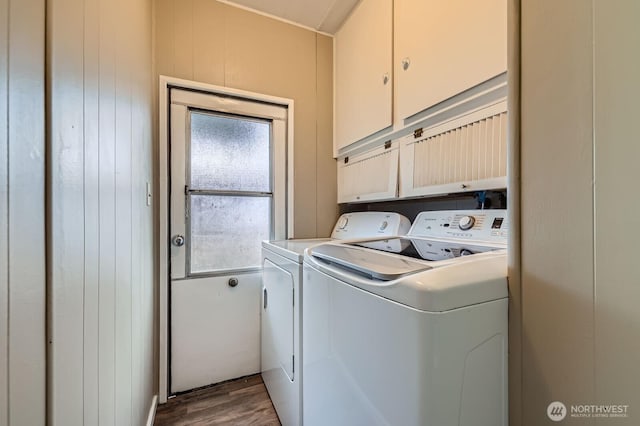 clothes washing area featuring wood finished floors, wooden walls, cabinet space, and washer and clothes dryer