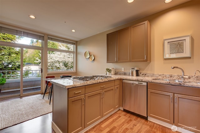 kitchen featuring light stone counters, recessed lighting, appliances with stainless steel finishes, a peninsula, and a sink