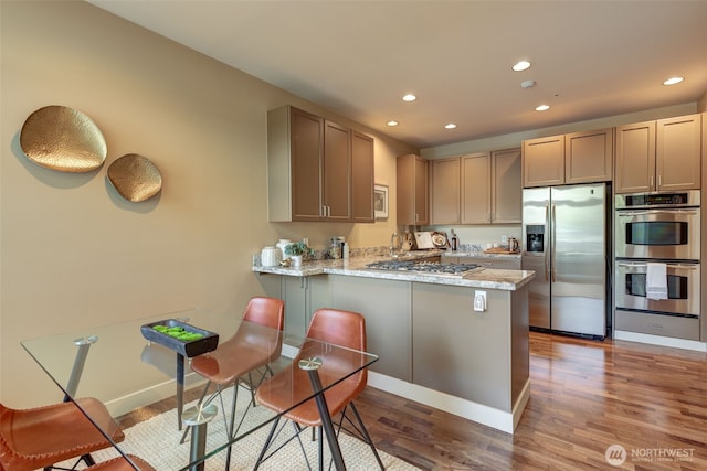 kitchen featuring a peninsula, recessed lighting, wood finished floors, and stainless steel appliances