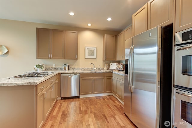 kitchen featuring recessed lighting, appliances with stainless steel finishes, a peninsula, light wood finished floors, and light stone countertops