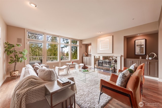 living area with a glass covered fireplace, baseboards, visible vents, and wood finished floors