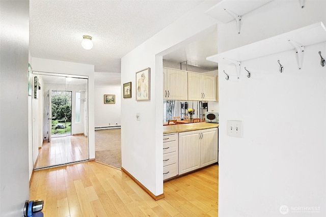 interior space with a baseboard radiator, a textured ceiling, light wood finished floors, and baseboards