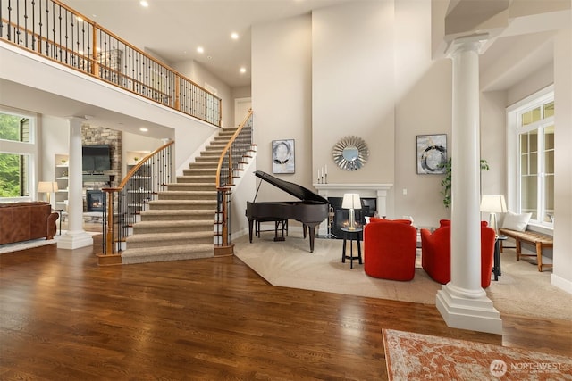 interior space featuring wood finished floors, decorative columns, stairs, a towering ceiling, and a glass covered fireplace