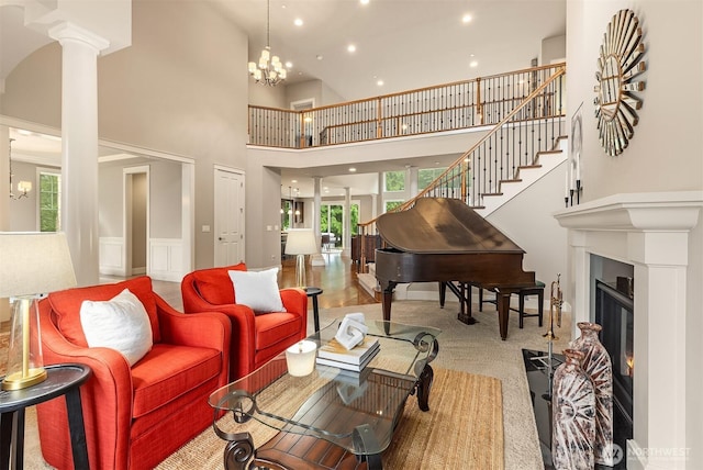carpeted living area with stairway, decorative columns, recessed lighting, a towering ceiling, and a glass covered fireplace