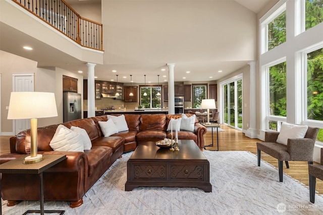living room with a wealth of natural light, decorative columns, a high ceiling, and light wood finished floors