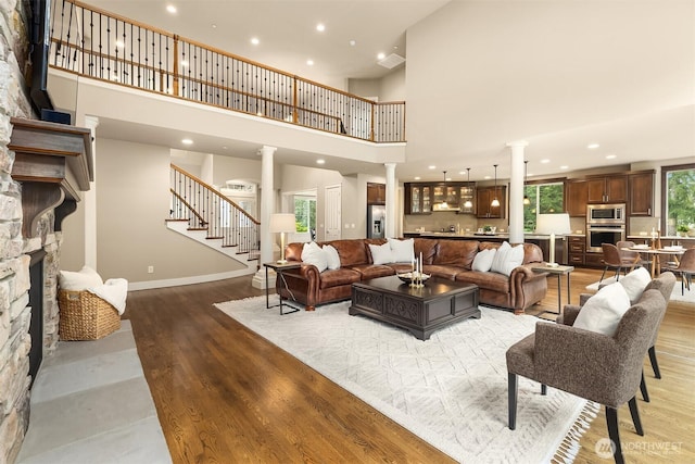 living area with stairway, a high ceiling, decorative columns, recessed lighting, and light wood-style floors