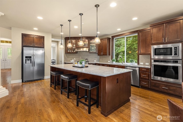 kitchen with stainless steel appliances, a breakfast bar area, wood finished floors, and decorative backsplash
