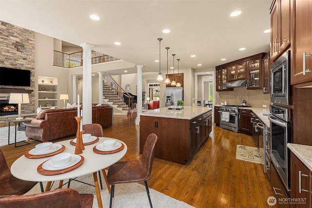 dining space with stairway, ornate columns, recessed lighting, a stone fireplace, and dark wood-type flooring