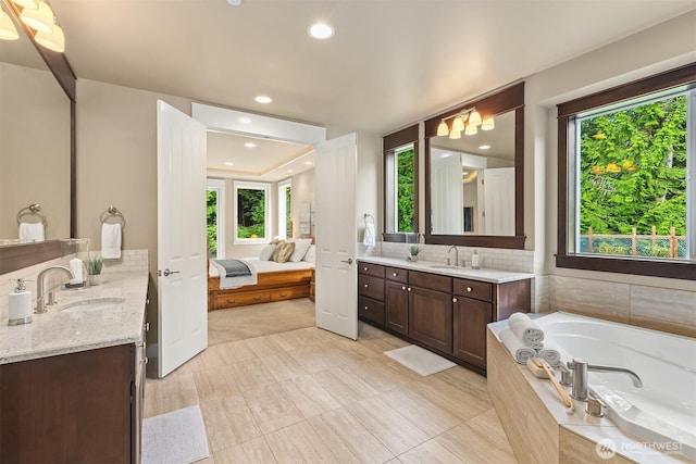 ensuite bathroom with a bath, ensuite bath, two vanities, and a sink