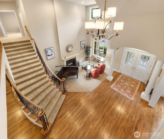foyer with a notable chandelier, a warm lit fireplace, wood finished floors, stairway, and a towering ceiling