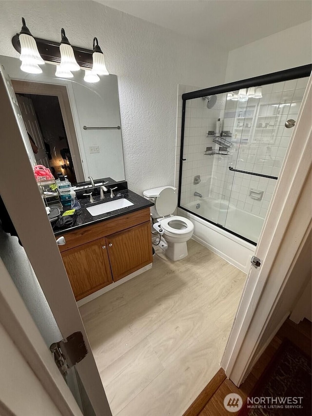 705 NE 143rd Ave Unit A1, Bellevue, WA 98007 - full bathroom with toilet, wood finished floors, combined bath / shower with glass door, a textured wall, and vanity
