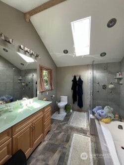 full bathroom with vanity, a garden tub, a shower stall, lofted ceiling with skylight, and toilet