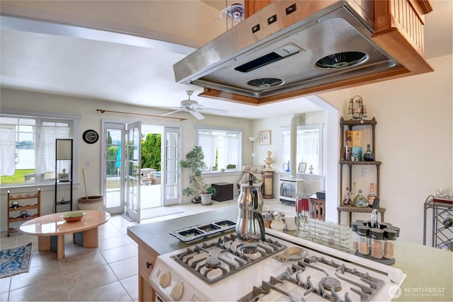 kitchen with light tile patterned flooring, white range with gas stovetop, ceiling fan, light countertops, and under cabinet range hood