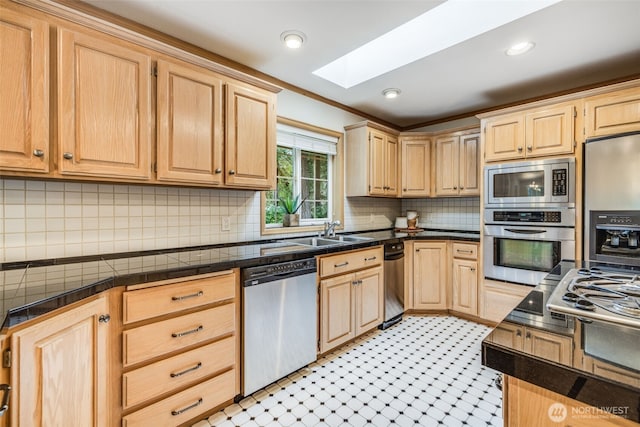 kitchen featuring a skylight, stainless steel appliances, light floors, light brown cabinets, and a sink