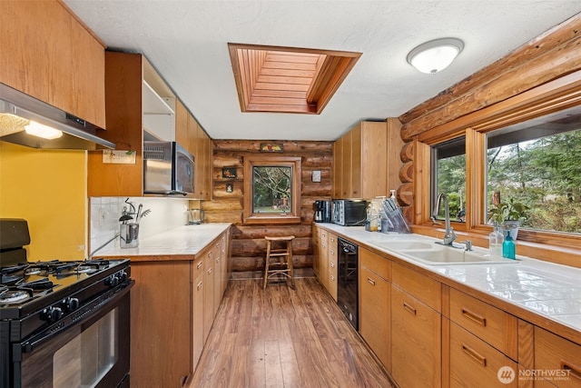 kitchen with light wood finished floors, stainless steel microwave, wine cooler, a sink, and black gas range