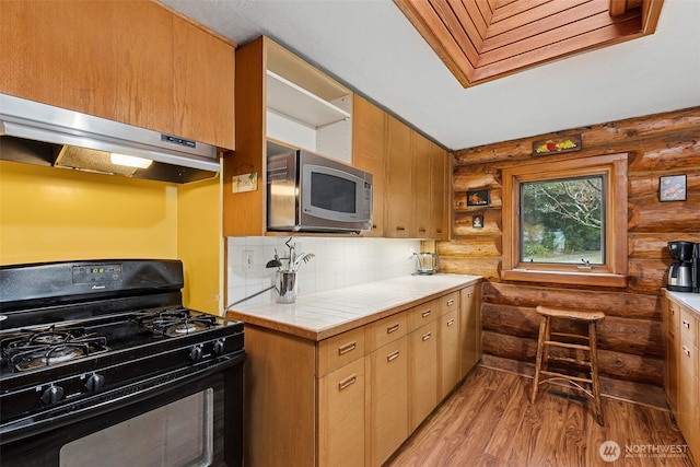 kitchen with decorative backsplash, light countertops, stainless steel microwave, under cabinet range hood, and black range with gas cooktop