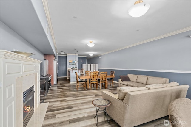 living room featuring a premium fireplace, baseboards, light wood-style floors, and ornamental molding